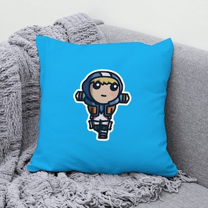 Può includere: Un cuscino blu con un'illustrazione di un personaggio dei cartoni animati che indossa una tuta blu e arancione e un casco. Il personaggio ha i capelli biondi e tiene un'arma.