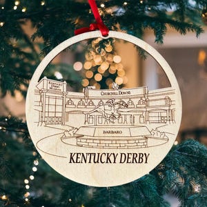 May include: A wooden Christmas ornament featuring a detailed illustration of Churchill Downs racetrack, the Kentucky Derby Museum, and a horse and jockey. The ornament is inscribed with "Kentucky Derby" and "Barbaro".