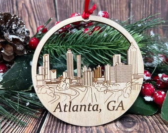 May include: A wooden Christmas ornament featuring a laser-cut design of the Atlanta, GA skyline. The ornament is round and has a brown wood finish.
