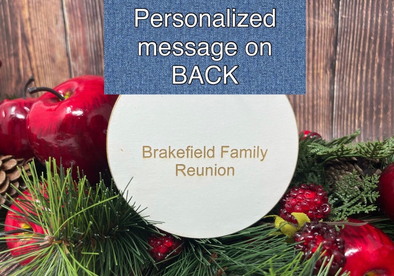 Puede incluir: Un letrero redondo de madera blanca con el texto "Brakefield Family Reunion" en letras doradas. El letrero est&aacute; rodeado de manzanas rojas, ramas de pino y bayas rojas.