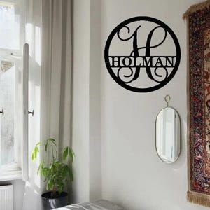 May include: Black metal circle with a decorative letter H and the name "HOLMAN" written across the center.