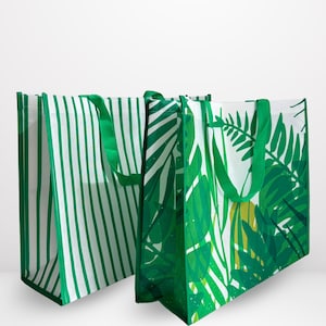 May include: Two reusable shopping bags with green and white designs. One bag features vertical green stripes, while the other showcases a vibrant green tropical leaf pattern. Both bags have green handles.