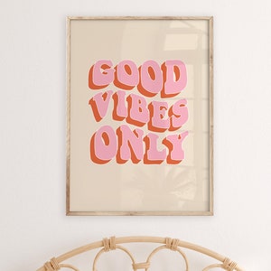 May include: A framed print with a beige background and the text "GOOD VIBES ONLY" in pink and orange letters. The print is hanging on a white wall above a wicker headboard.