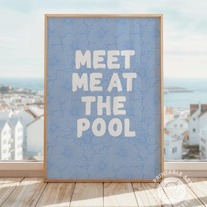 Peut inclure: Une affiche encadrée avec le texte "MEET ME AT THE POOL" en lettres blanches. Le fond est bleu clair avec un motif floral. Le cadre est de couleur marron clair. L'affiche est présentée sur une surface en bois.