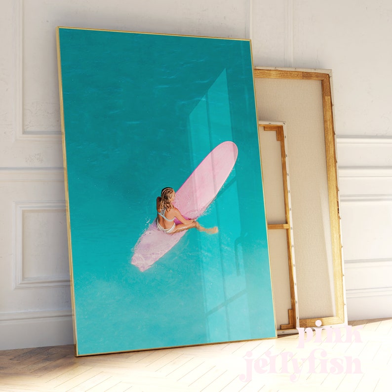 May include: A woman in a white bikini sits on a pink surfboard in turquoise water.