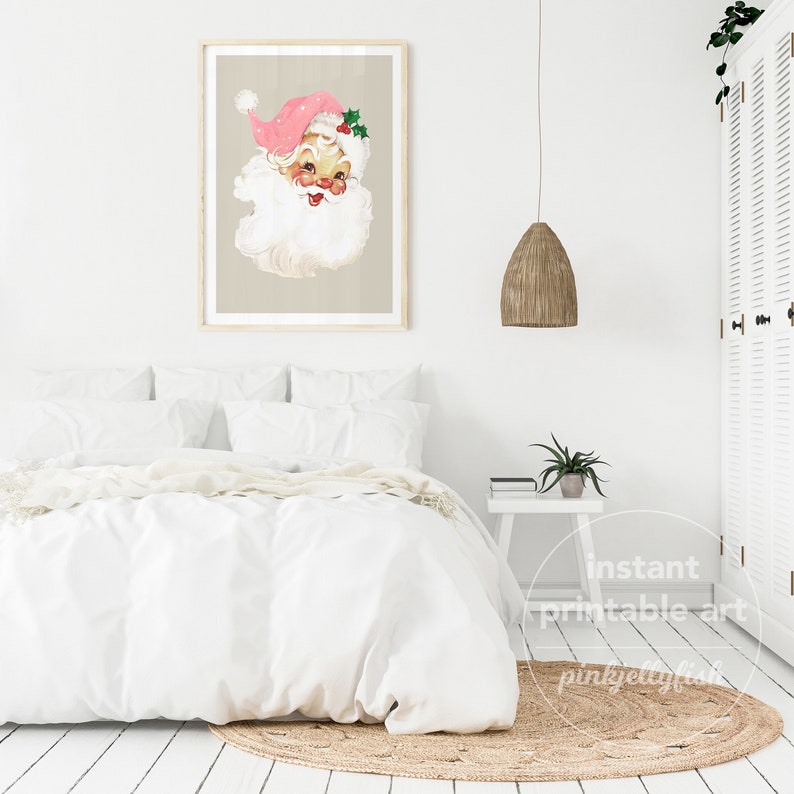 May include: A printable art print featuring a vintage illustration of Father Christmas with a pink hat and a white beard. The print is framed and hanging on a white wall above a white bed with a white duvet and pillows.