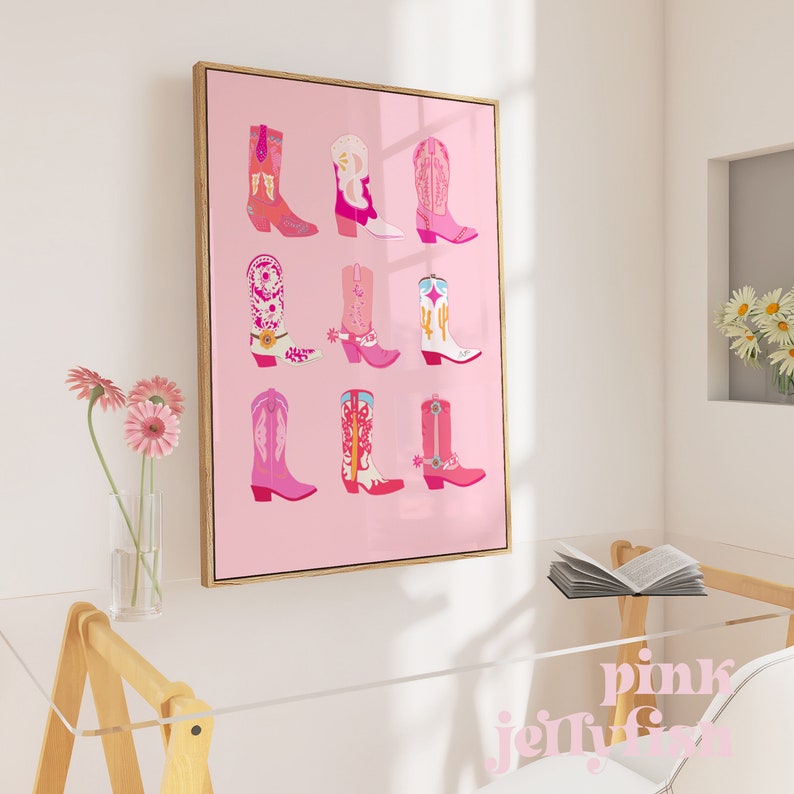May include: A framed art print featuring nine colorful cowboy boots in shades of pink, red, and white against a pink background. The boots have various designs, including floral patterns and stars. The frame is a light brown color.