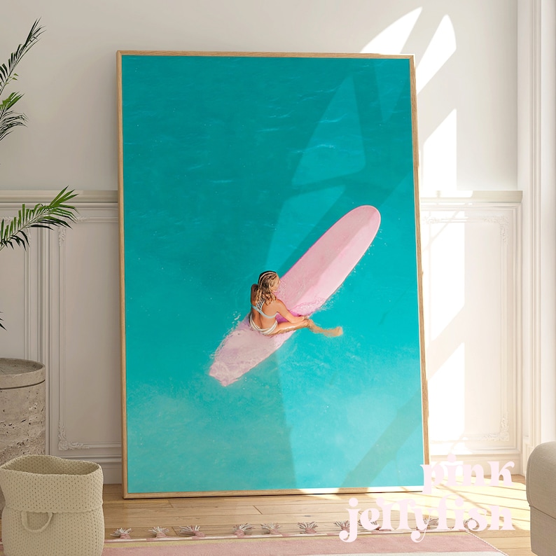 May include: A woman sits on a pink surfboard in turquoise water. The surfboard is floating on the surface of the water. The woman is wearing a bikini and has her hair pulled back.