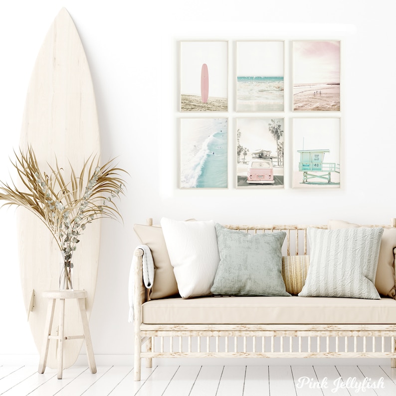 May include: A set of six framed prints with a beach theme. The prints feature a pink surfboard, a beach scene with waves, a pink car, and a lifeguard stand. The prints are arranged in a grid pattern on a white wall.