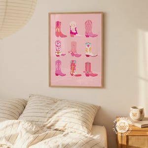 May include: A framed print featuring nine colorful illustrations of cowboy boots in various designs. The boots are primarily pink, with accents of white, yellow, and blue. The artwork is set against a soft pink background.