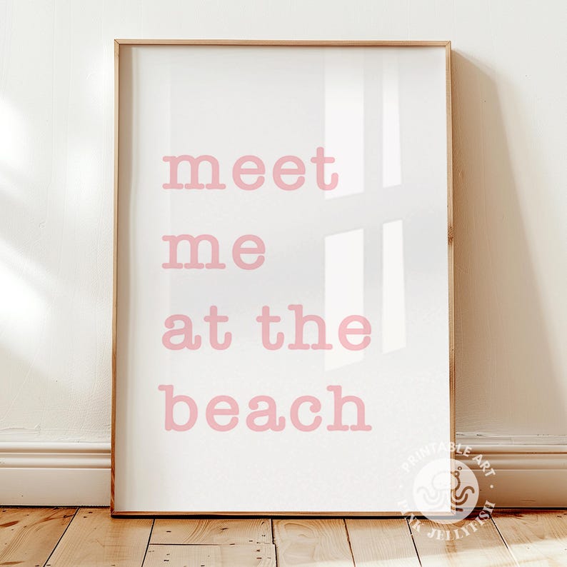 Puede incluir: Una impresi&oacute;n enmarcada con las palabras "meet me at the beach" en letras rosas sobre un fondo blanco. La impresi&oacute;n est&aacute; en un marco de madera clara y se muestra sobre una superficie de madera.