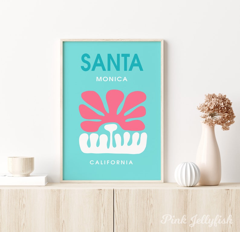 May include: A turquoise blue poster with the text "SANTA MONICA CALIFORNIA" in white lettering. A pink stylized flower with a white stem is in the center of the poster.
