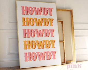 Op de afbeelding: Een witte canvas print met een gouden lijst met het woord "HOWDY" vijf keer herhaald in een roze en oranje lettertype.