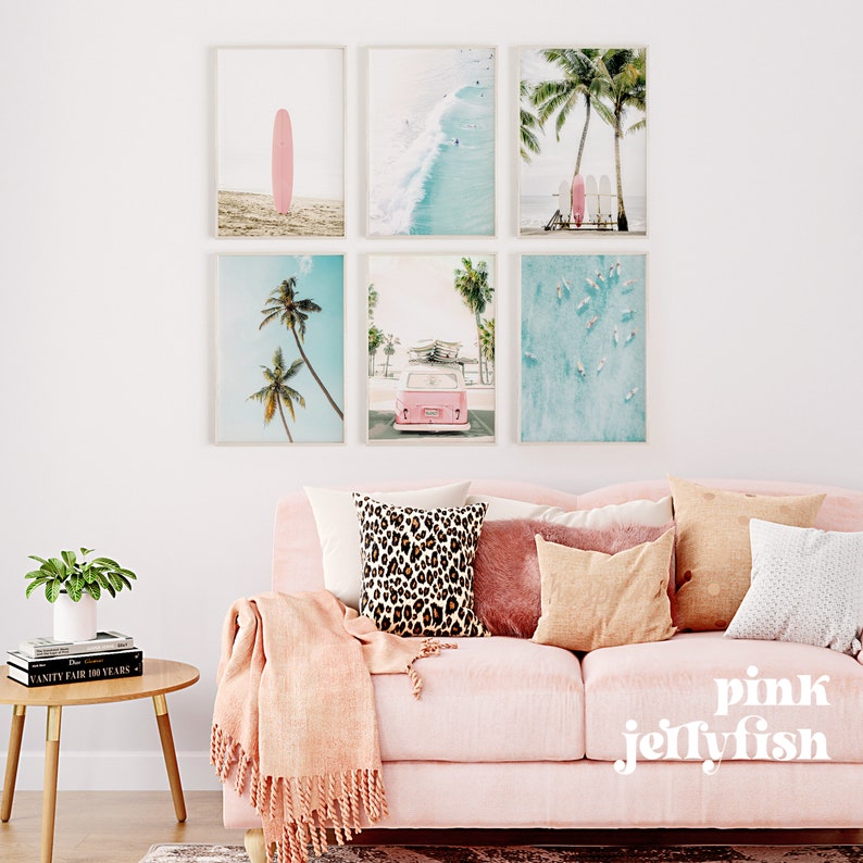 May include: Six framed prints with a beach theme. The prints feature palm trees, surfboards, a pink van, and a turquoise ocean. The prints are arranged in a grid pattern on a white wall above a pink sofa with throw pillows.