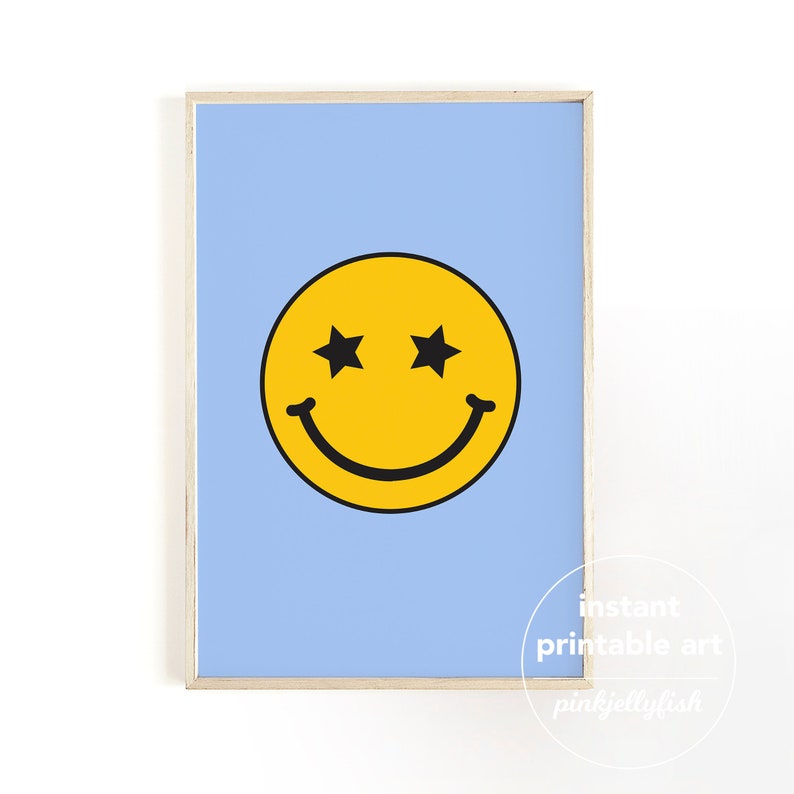 May include: A framed print with a yellow smiley face with star-shaped eyes on a pale blue background. The smiley face has a black outline and a curved smile. The frame is a light wood colour. Text in the lower right corner reads "instant printable art".