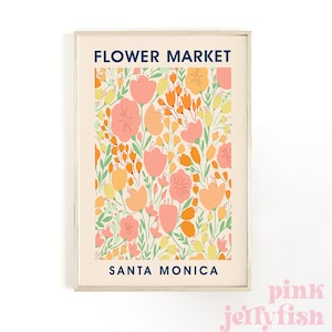 May include: A framed art print featuring a floral pattern in shades of peach, orange, yellow, and green on a cream background. The words "FLOWER MARKET" and "SANTA MONICA" are printed in navy blue. The print is in a light wood frame.