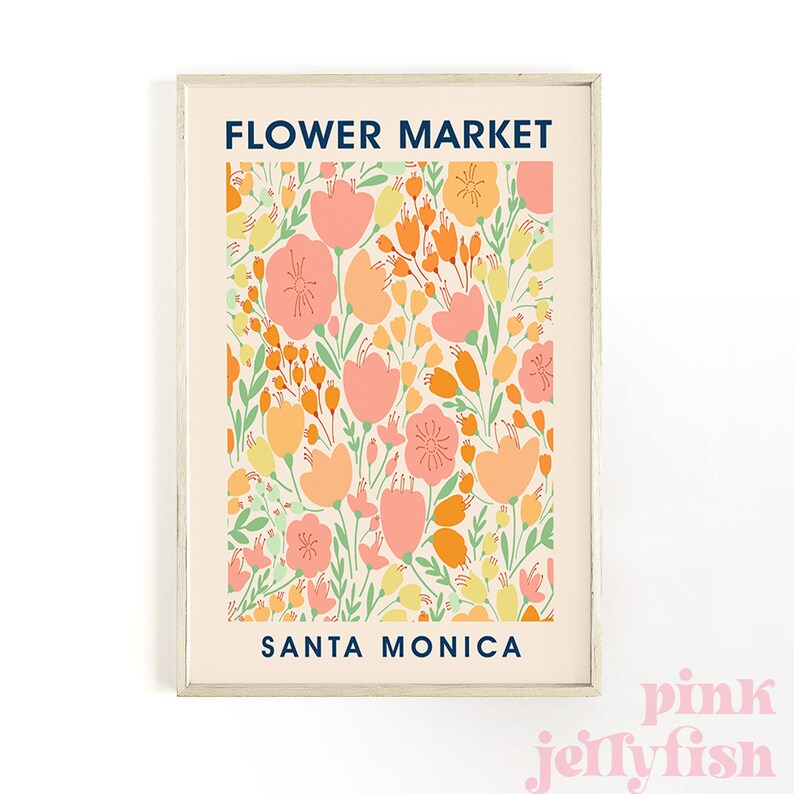 May include: A framed art print featuring a floral pattern in shades of peach, orange, yellow, and green on a cream background. The words "FLOWER MARKET" and "SANTA MONICA" are printed in navy blue. The print is in a light wood frame.