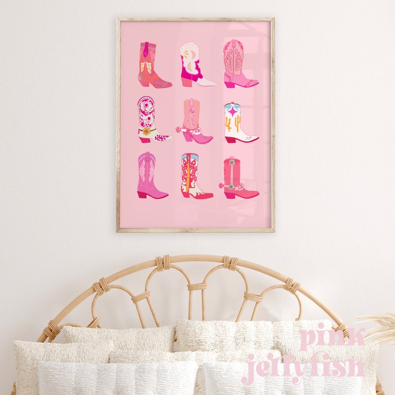 May include: A framed print featuring nine colorful cowboy boots in shades of pink, orange, and white, set against a pink background. The boots showcase various designs, including floral patterns and cactus motifs. The print is displayed above a bed with a woven headboard.