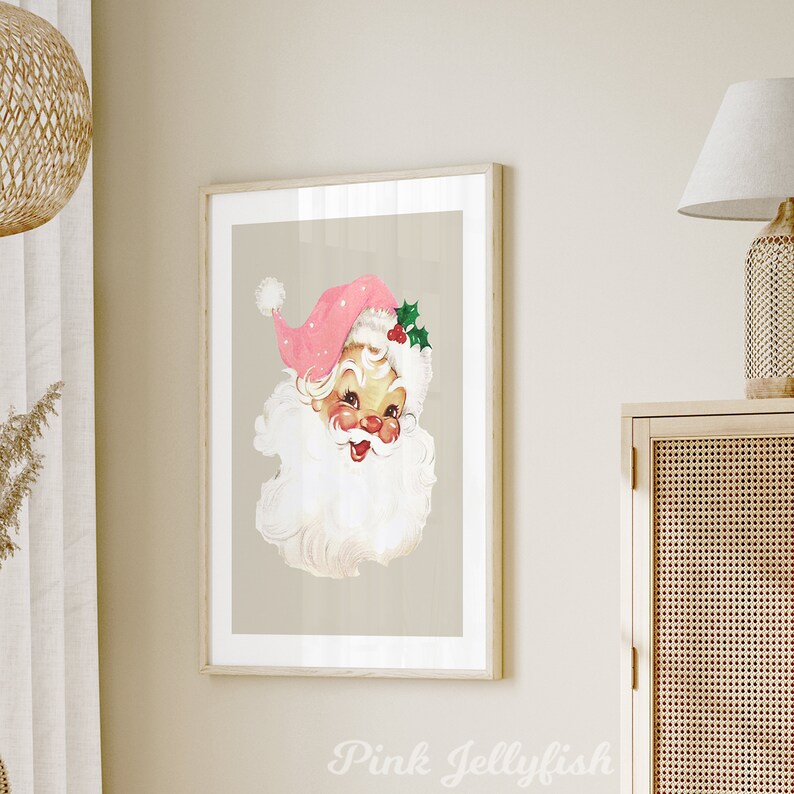 May include: A vintage illustration of Father Christmas with a pink hat and white beard. The illustration is framed in a light wood frame and has a beige background.