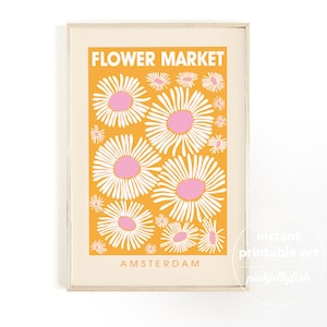 May include: A framed art print featuring a retro-style design. The print has a bright orange background with white and pink daisy illustrations. The words "FLOWER MARKET" and "AMSTERDAM" are printed on the art print.