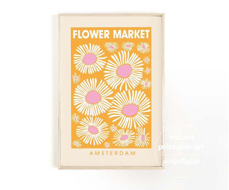 May include: A framed art print featuring a retro-style design. The print has a bright orange background with white and pink daisy illustrations. The words "FLOWER MARKET" and "AMSTERDAM" are printed on the art print.