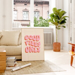 May include: A framed print with a beige background and the text "GOOD VIBES ONLY" in pink and orange letters. The letters are in a retro, 3D style.