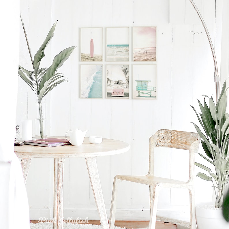 May include: A set of six framed prints with a beach theme. The prints feature a pink surfboard, a beach scene with palm trees, a lifeguard stand, and a pink vintage car. The prints are arranged in a grid pattern on a white wall.
