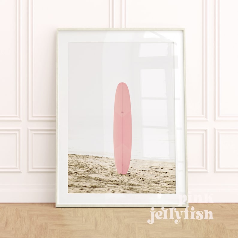 May include: A pink surfboard standing upright on a sandy beach. The surfboard is a longboard style with a rounded nose and a single fin.