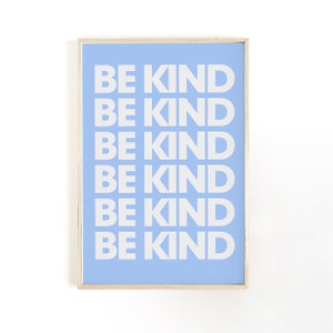 May include: A framed art print featuring the words "BE KIND" in white, repeated on a light blue background. The frame is a light wood colour. The print is centered on a white background.