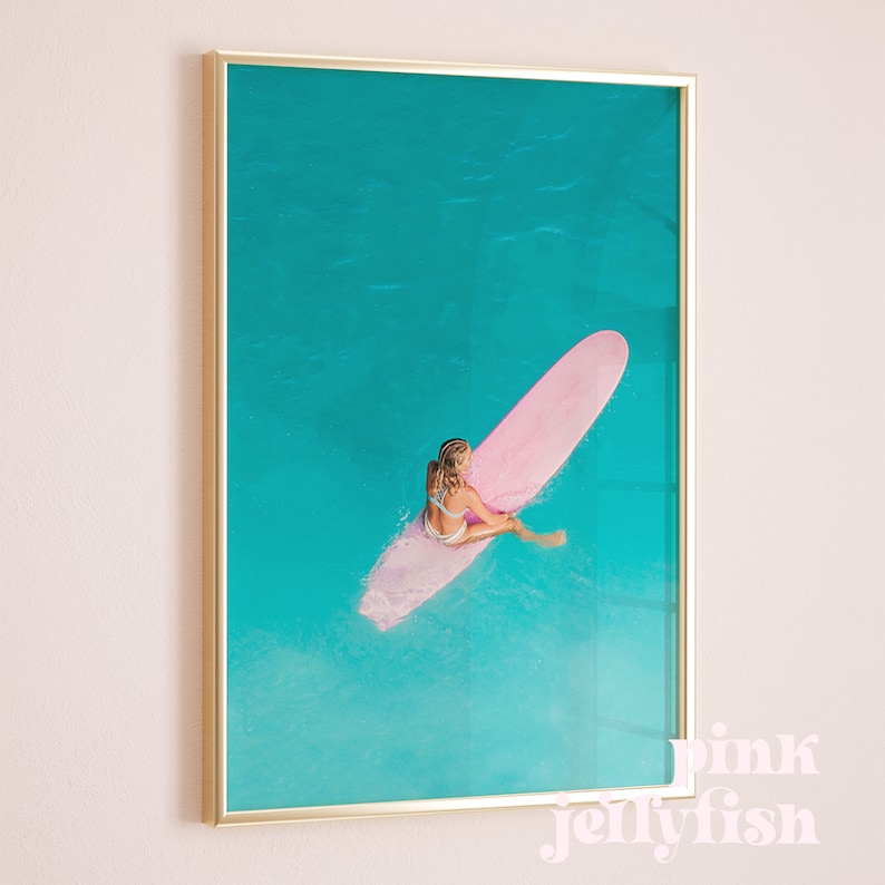 May include: A woman sits on a pink surfboard in turquoise water. The surfboard is partially submerged in the water. The woman is wearing a white bikini top and a blue bikini bottom. The water is clear and blue.