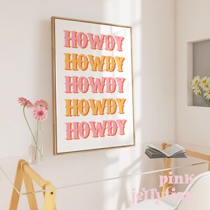 May include: A framed print with the word "Howdy" repeated five times in a pink and orange color scheme. The print is on a white background and has a wooden frame.