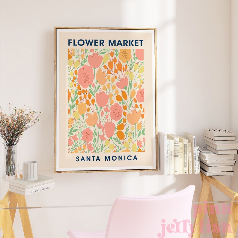 May include: A framed art print with a floral design. The print features a cream-colored background with a pattern of pink, orange, and yellow flowers and green leaves. The text "FLOWER MARKET SANTA MONICA" is displayed in navy blue.