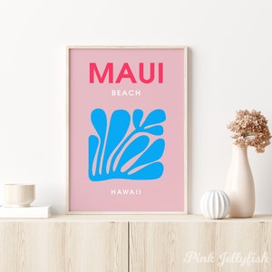 May include: A pink and white poster with the text "MAUI BEACH HAWAII" in bold red and white lettering. A blue stylized floral design is in the center of the poster.