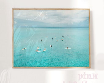 May include: A framed photograph of a group of people paddleboarding on a turquoise ocean. The sky is a light blue with white clouds. The photo is taken from a high angle, looking down on the water.