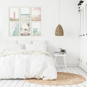 May include: A white bedroom with a bed, a white nightstand, a hanging light fixture, and a jute rug. Six framed prints of beach scenes hang on the wall above the bed.