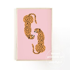 Pode incluir: Dois guepardos laranja e preto se encarando em um fundo rosa. Os guepardos est&atilde;o em um estilo de design gr&aacute;fico estilizado. A imagem &eacute; emoldurada com uma moldura de madeira clara.