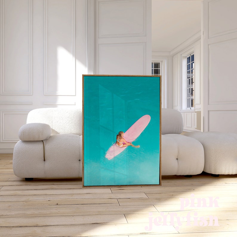 May include: A framed photograph of a person on a pink surfboard in turquoise water.
