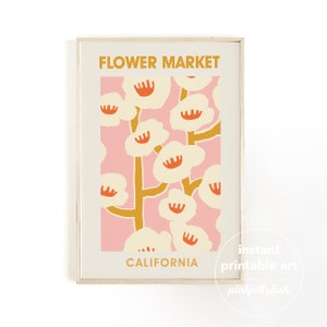May include: A framed art print featuring a floral design with the words "Flower Market" and "California". The artwork showcases cream-colored flowers with orange centers against a pink background, with mustard-colored stems. The print is in a light wood frame.
