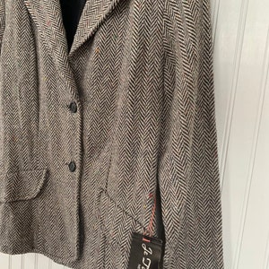 Op de afbeelding: Een zwart-witte herringbone blazer met een enkele knoopsluiting en een zak aan de linkerkant. De blazer heeft een label met de tekst "Je Taime Ltd. New York, N.Y."
