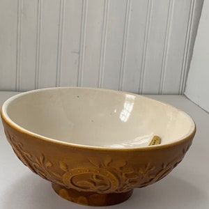 May include: A brown ceramic bowl with a white interior and an embossed floral design. The bowl has a footed base.
