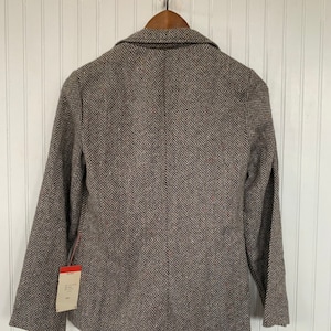 Op de afbeelding: Een bruin en zwart herringbone blazer met een label aan de mouw.