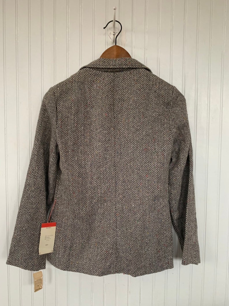 Op de afbeelding: Een bruin en zwart herringbone blazer met een label aan de mouw.