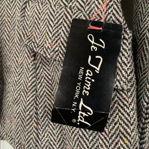Op de afbeelding: Een zwart-witte stof met een herringbone-patroon en een klein label met de tekst "Je T'aime Ltd. New York, N.Y."