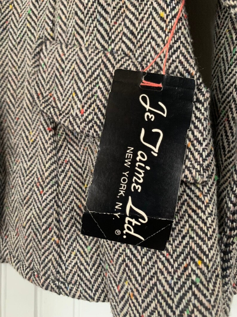 Op de afbeelding: Een zwart-witte stof met een herringbone-patroon en een klein label met de tekst "Je T'aime Ltd. New York, N.Y."