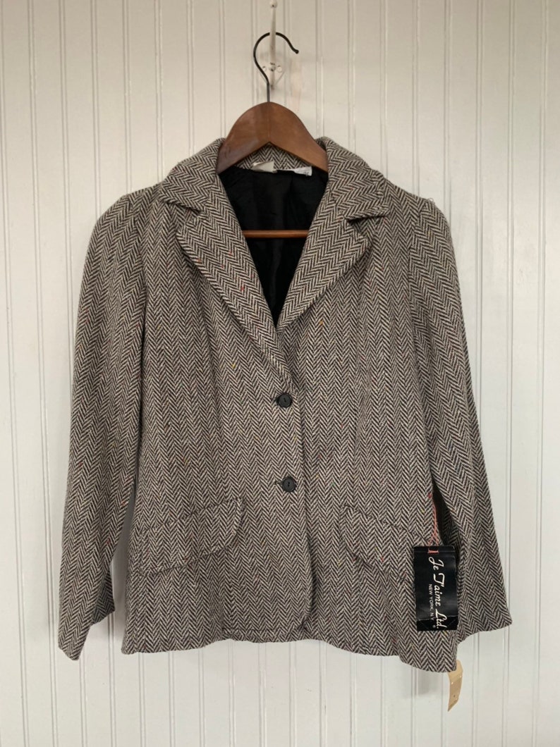 Op de afbeelding: Een bruin en wit herringbone blazer met een zwarte voering en drie zwarte knopen. De blazer heeft een zak aan de linkerkant en een label met de tekst "J'aime Ltd."