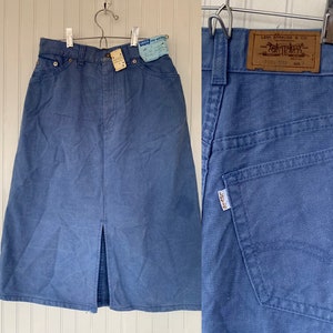 May include: A blue denim skirt with a front slit and a Levi's label on the back. The skirt has a high waist and a straight fit.