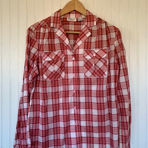 May include: A long-sleeved button-down shirt with a red, white, and blue plaid pattern. The shirt has two chest pockets and a collared neckline. The brand name "Jantzen" is visible on the label.