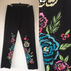 May include: Black pants with colorful floral embroidery on the legs. The embroidery features flowers, leaves, and beads.