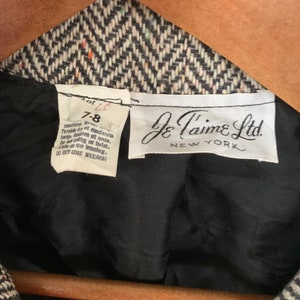 Op de afbeelding: Een zwart-witte herringbone blazer met een zwarte voering. Het label vermeldt "Je T'aime Ltd. New York" en "Lot 7-8". De wasinstructies zijn: machinewas, drogen in de droger op lage temperatuur, strijken op lage temperatuur, niet wringen of draaien, niet chemisch reinigen, geen bleekmiddel gebruiken.