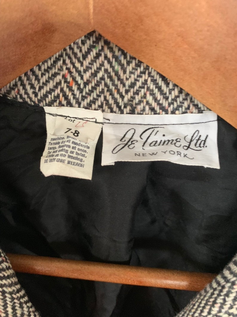 Op de afbeelding: Een zwart-witte herringbone blazer met een zwarte voering. Het label vermeldt "Je T'aime Ltd. New York" en "Lot 7-8". De wasinstructies zijn: machinewas, drogen in de droger op lage temperatuur, strijken op lage temperatuur, niet wringen of draaien, niet chemisch reinigen, geen bleekmiddel gebruiken.